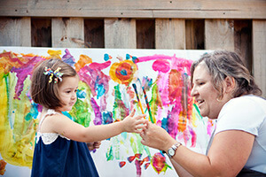 Woman with young girl holding paint brushes in front of a painting