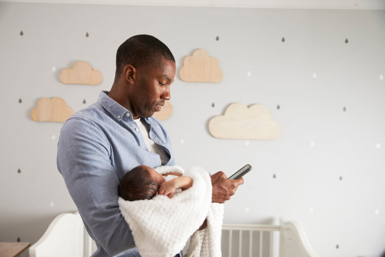 Father Holding Newborn Baby Son Using Mobile Phone