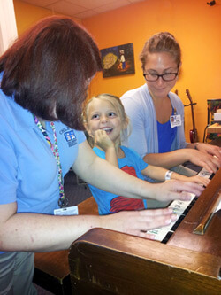Smiling little girl playing piano with two female therapists