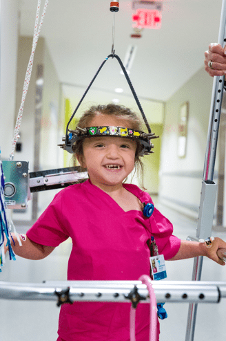 child holding onto bars as she walks with head stabilizing gear