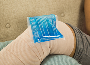 Closeup of knee wrapped in bandage, lying on pillow with ice pack on top.